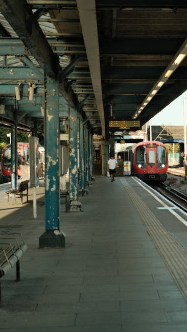The exterior of Wembley Park Station entrance with a large sign displaying the station's name in bold letters against a cloudy sky. The station features a covered walkway with dark metal supports and a roof. Below the sign, there are multiple staircases leading down to the station platform, with a group of people ascending and descending. Some individuals are wearing face masks, carrying backpacks or bags, and dressed in casual clothing. The image captures the urban environment of a busy travel hub associated with house relocations and moving logistics, emphasizing transportation services near Finsbury Park and potential furniture transport activities involved in home removals or packing and moving tasks managed by Man and a Van Finsbury Park.