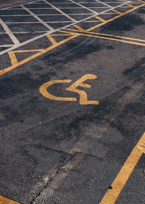 Close-up image of a disabled parking bay on an asphalt surface, featuring a yellow disabled access symbol painted on the ground. The parking bay has diagonal yellow stripes at its edges, indicating re